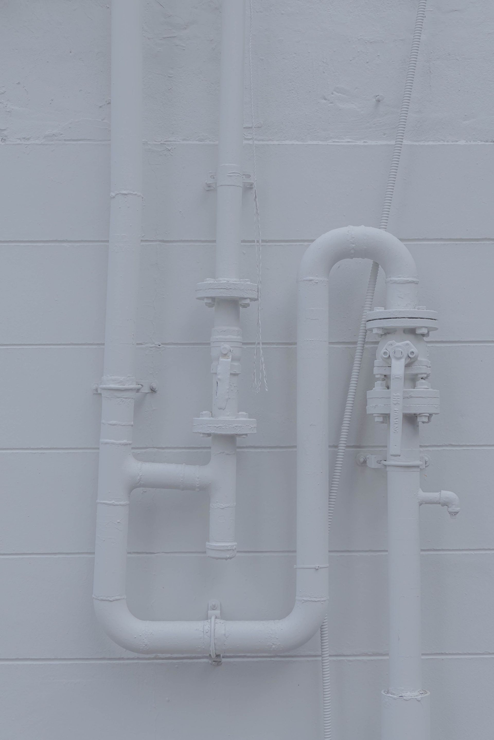 Close-up of white industrial pipes on a wall, showcasing minimalistic design.