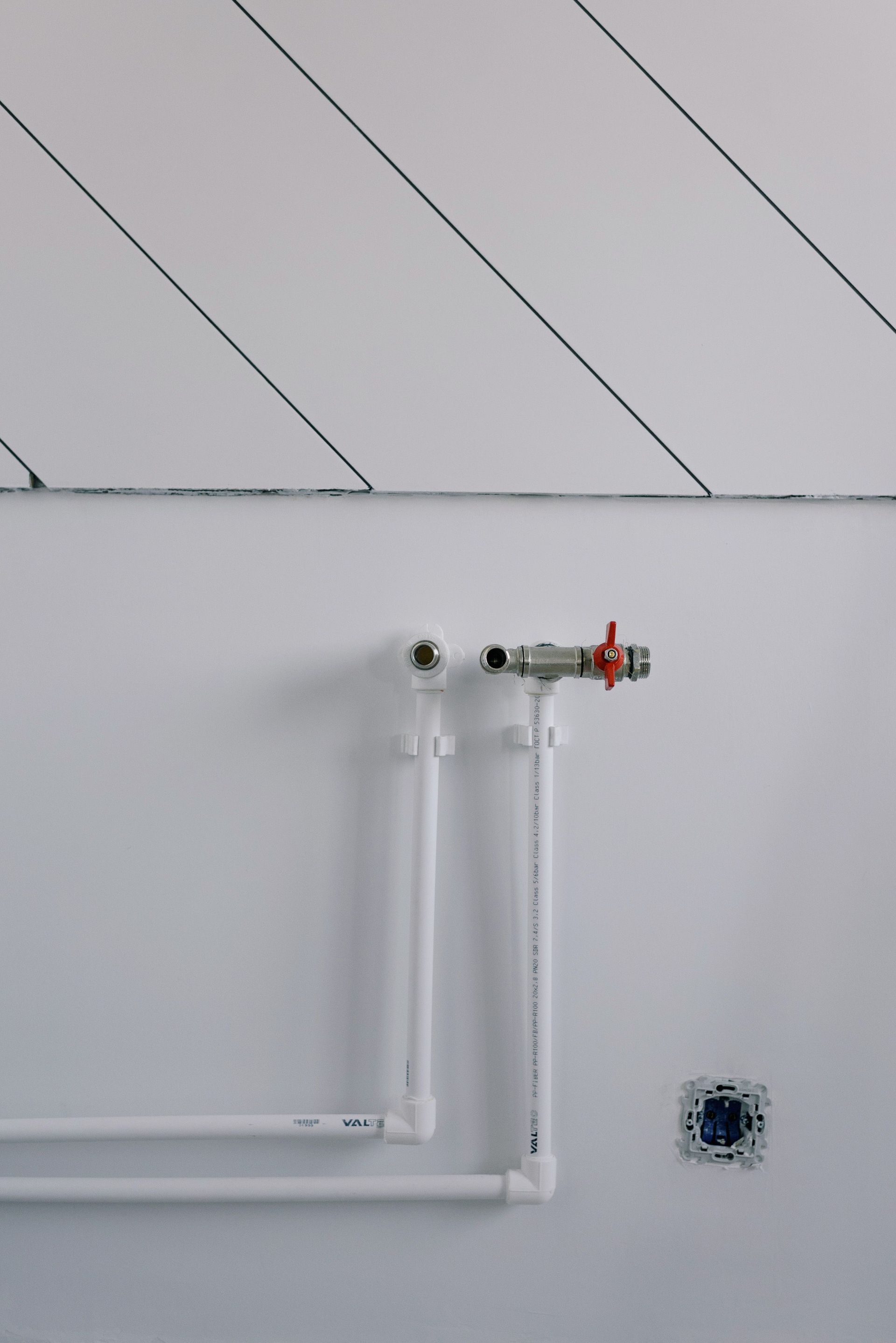 Long thin black slanted lines over pipes of radiator casting shadow on white wall in daytime